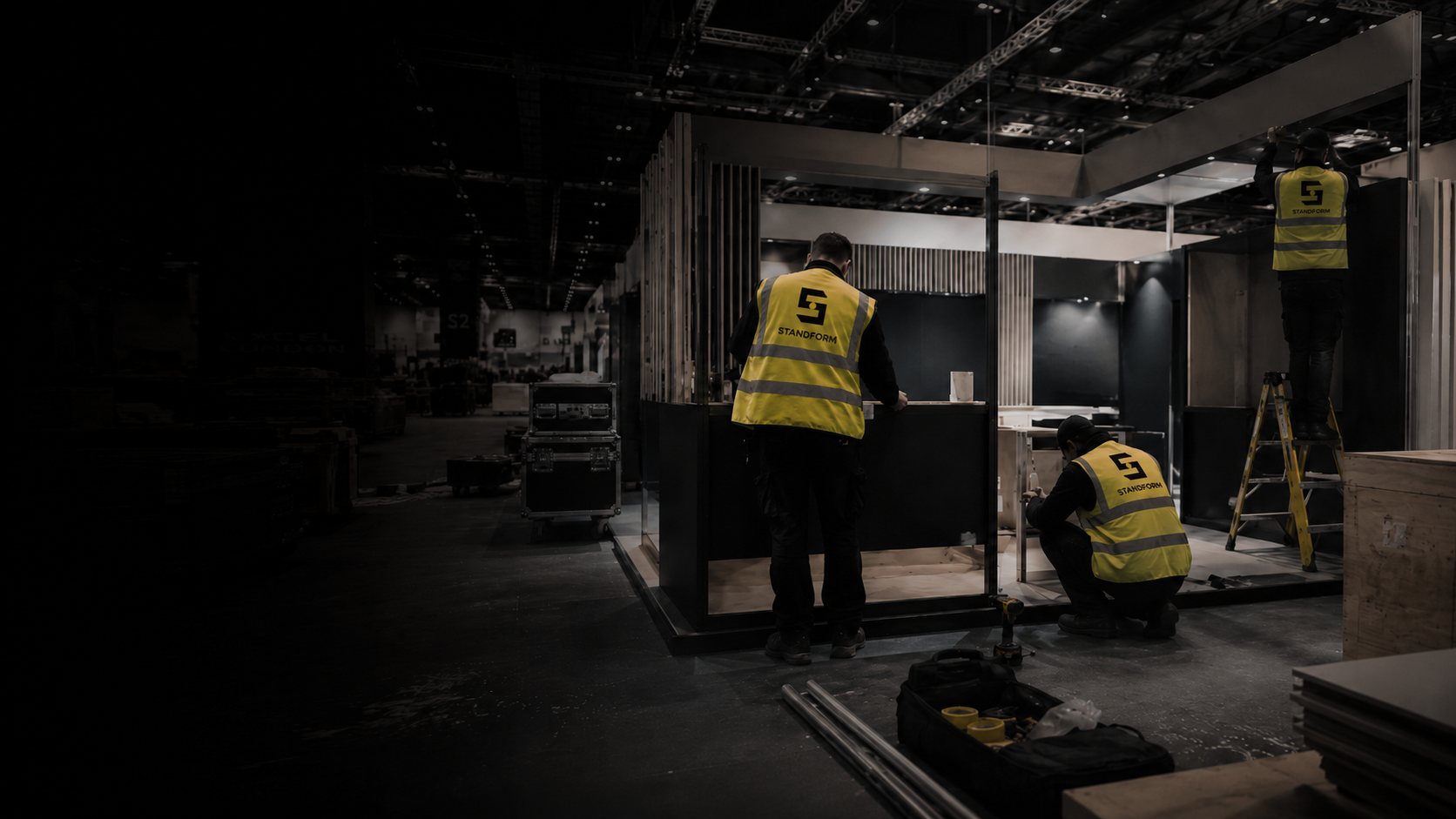 Standform crew in yellow hi-vis vests installing an exhibition stand in a dark exhibition hall before the show opens
